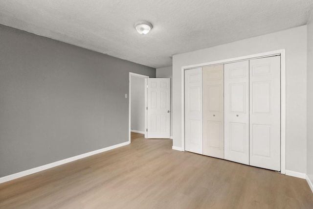 unfurnished bedroom with a textured ceiling, a closet, light wood-type flooring, and baseboards