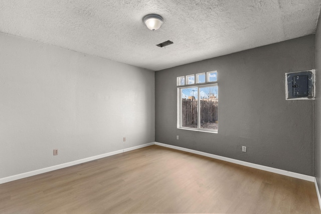 empty room with electric panel, visible vents, baseboards, wood finished floors, and a textured ceiling