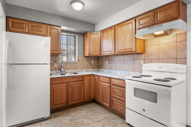 kitchen featuring under cabinet range hood, white appliances, a sink, brown cabinets, and tasteful backsplash