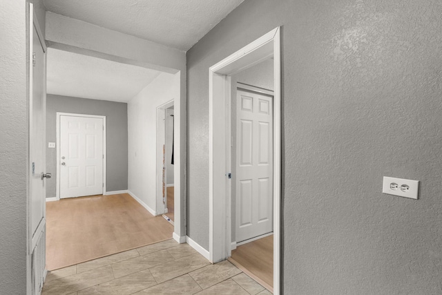 hall with a textured wall, a textured ceiling, and baseboards