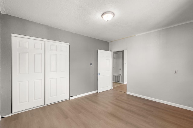 unfurnished bedroom featuring a closet, visible vents, baseboards, and wood finished floors