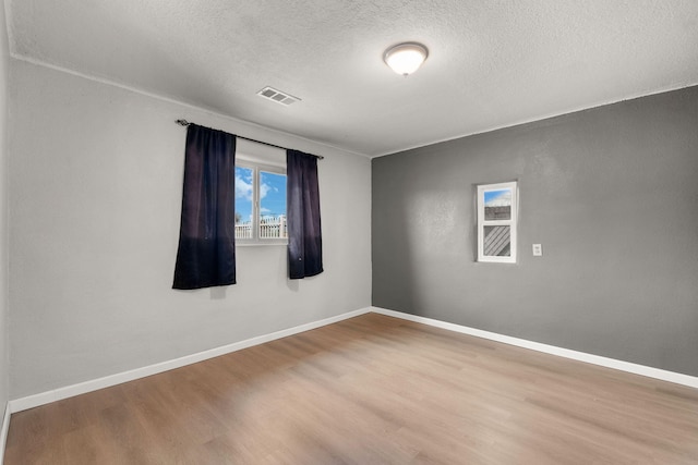 empty room with baseboards, a textured ceiling, visible vents, and wood finished floors