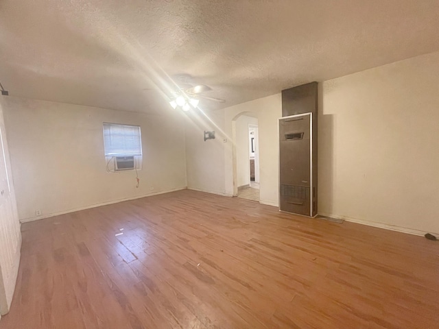 additional living space with arched walkways, a ceiling fan, light wood-style flooring, cooling unit, and a textured ceiling