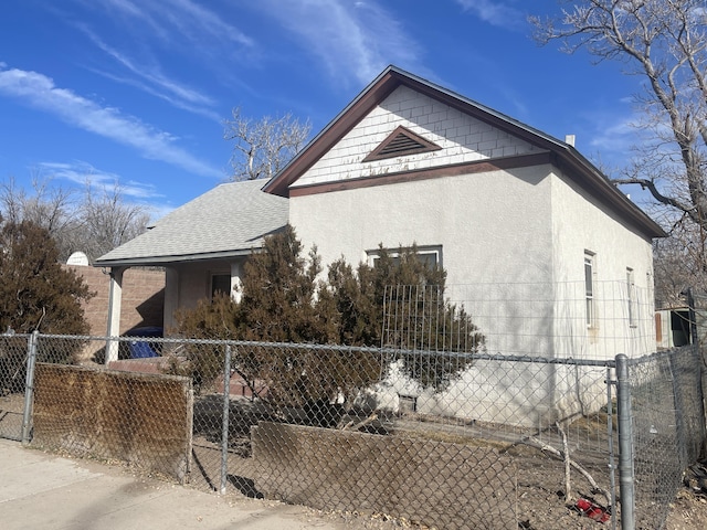 view of side of property with a fenced front yard, a shingled roof, and stucco siding