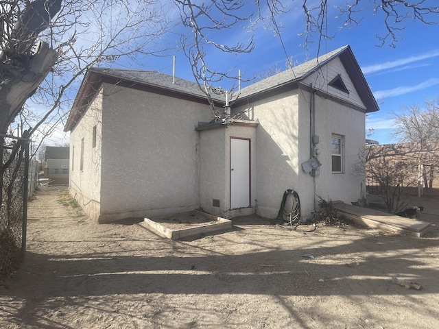 rear view of property featuring roof with shingles, fence, and stucco siding