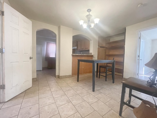 kitchen with light tile patterned floors, arched walkways, freestanding refrigerator, a peninsula, and a chandelier