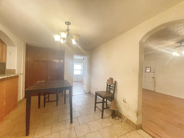 dining space with arched walkways, light tile patterned floors, a textured ceiling, baseboards, and an inviting chandelier