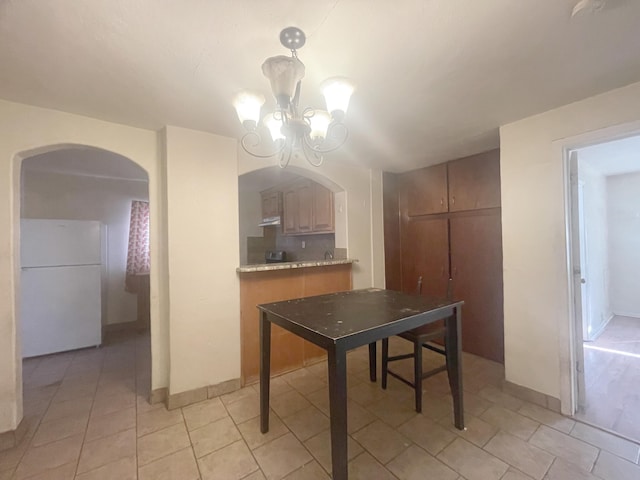 dining space with a chandelier, arched walkways, baseboards, and light tile patterned floors