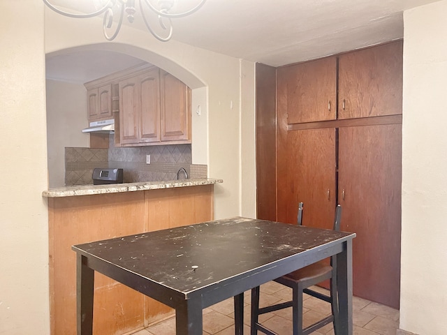 kitchen featuring light tile patterned floors, tasteful backsplash, a sink, and under cabinet range hood