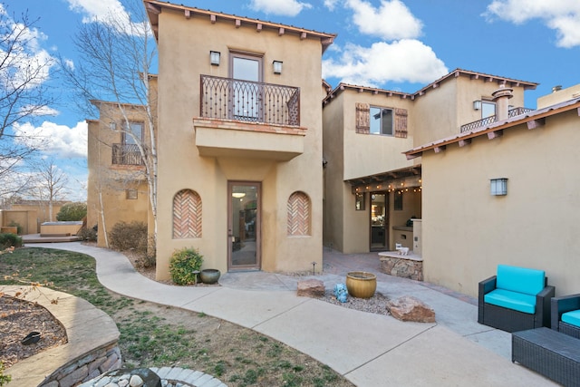 rear view of house featuring a patio area, a balcony, and stucco siding