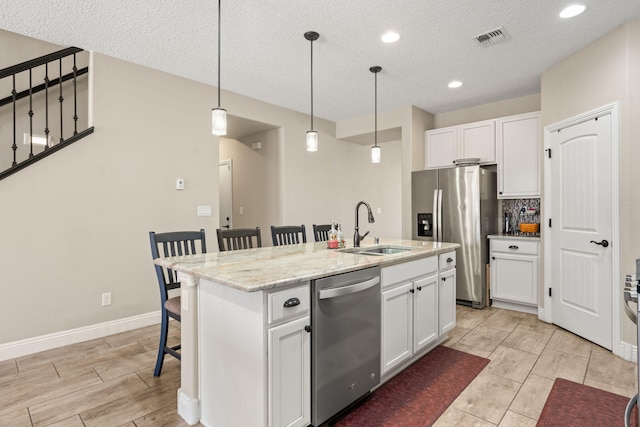 kitchen featuring visible vents, appliances with stainless steel finishes, white cabinets, a sink, and a kitchen breakfast bar