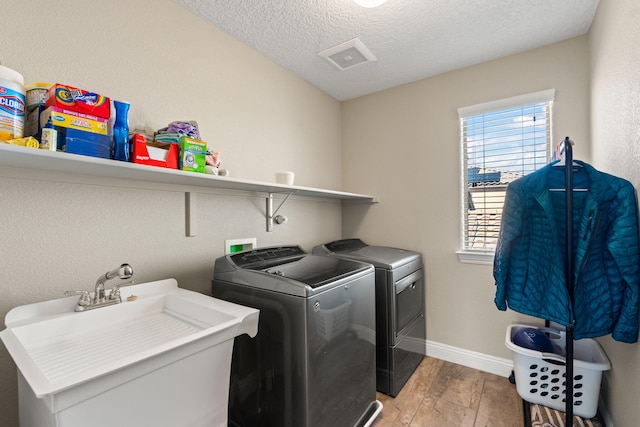 laundry area with a sink, a textured ceiling, wood finished floors, washer and dryer, and laundry area