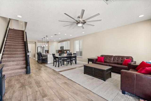 living area with visible vents, a textured ceiling, stairway, and a ceiling fan