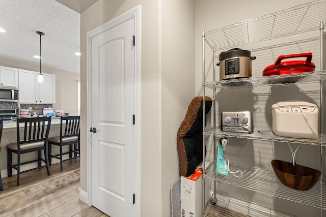 interior space with white cabinetry, a kitchen breakfast bar, light wood-style floors, backsplash, and stainless steel microwave