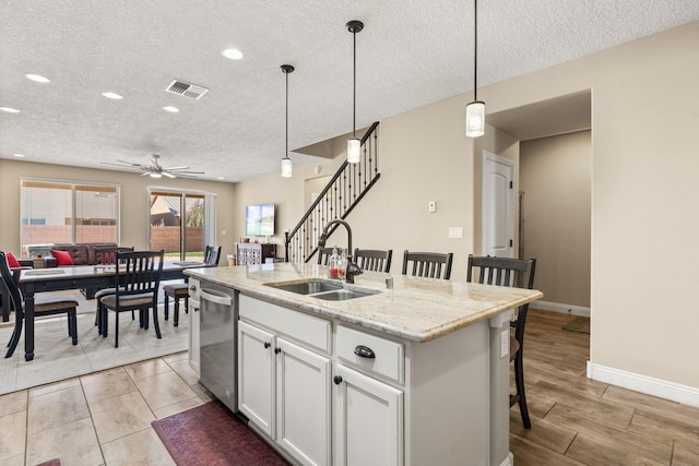 kitchen featuring visible vents, dishwasher, a breakfast bar area, hanging light fixtures, and a sink