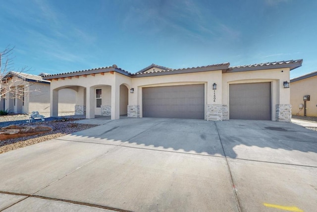 mediterranean / spanish-style house with stucco siding, a garage, stone siding, driveway, and a tiled roof