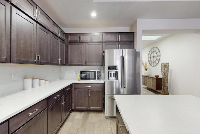 kitchen with stainless steel appliances, dark brown cabinets, light countertops, and light wood-style floors