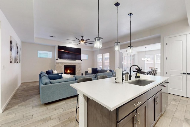 kitchen with a stone fireplace, a sink, light countertops, an island with sink, and decorative light fixtures