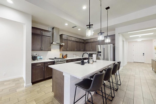 kitchen featuring premium appliances, decorative light fixtures, light countertops, a sink, and wall chimney exhaust hood