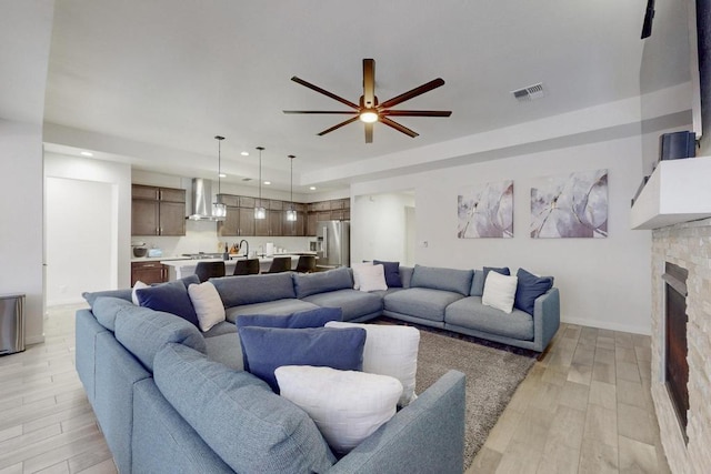 living room featuring light wood-type flooring, visible vents, a stone fireplace, and recessed lighting