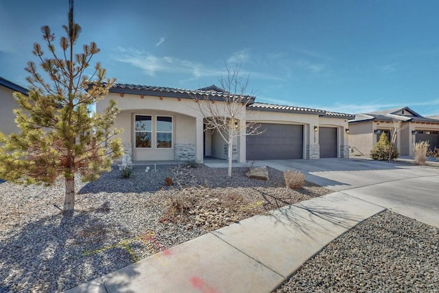 mediterranean / spanish home with stone siding, stucco siding, an attached garage, and concrete driveway