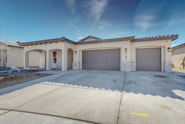 mediterranean / spanish home with a tile roof, stucco siding, an attached garage, stone siding, and driveway