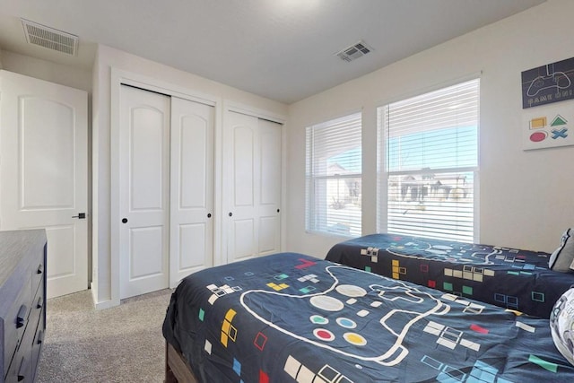 bedroom with light carpet, two closets, and visible vents