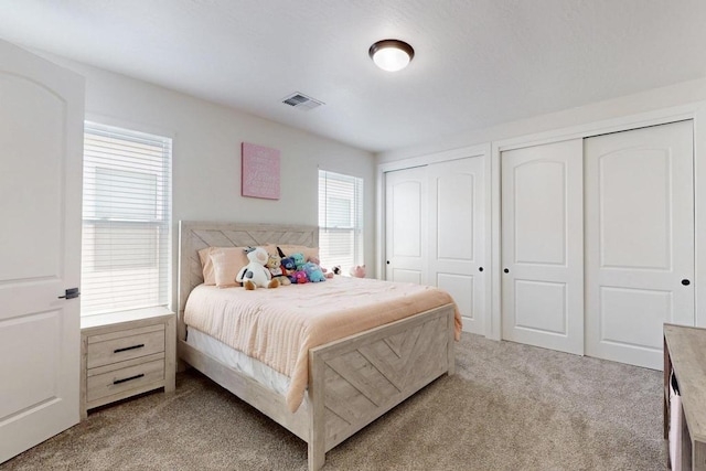 bedroom with light carpet, multiple windows, visible vents, and multiple closets