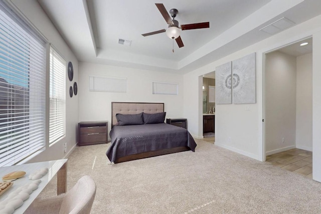 bedroom featuring light carpet, a tray ceiling, visible vents, and baseboards