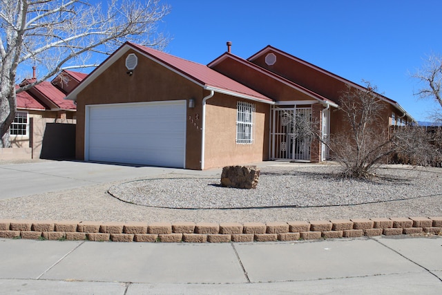 ranch-style home featuring an attached garage, metal roof, concrete driveway, and stucco siding