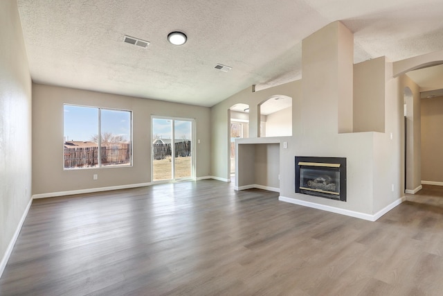 unfurnished living room with a glass covered fireplace, visible vents, baseboards, and wood finished floors