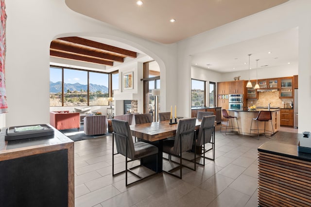 dining space featuring arched walkways, beam ceiling, recessed lighting, a glass covered fireplace, and a mountain view