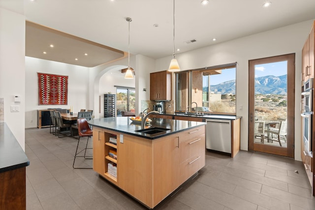 kitchen with tasteful backsplash, dark countertops, appliances with stainless steel finishes, hanging light fixtures, and a kitchen island with sink