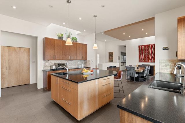 kitchen with dark countertops, a center island with sink, pendant lighting, and a sink