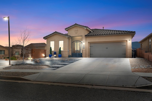 mediterranean / spanish-style house with a garage, concrete driveway, a gate, and stucco siding