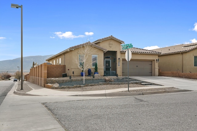 view of front of home with an attached garage, a mountain view, fence, driveway, and stucco siding