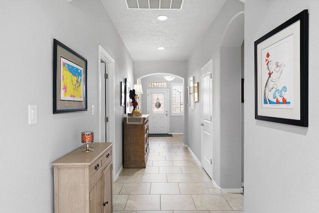 hall featuring arched walkways, a textured ceiling, light tile patterned flooring, visible vents, and baseboards