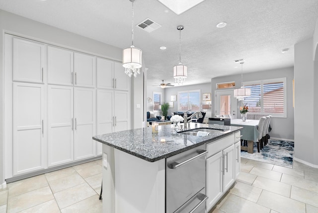 kitchen featuring visible vents, white cabinets, dark stone countertops, a kitchen island with sink, and a sink