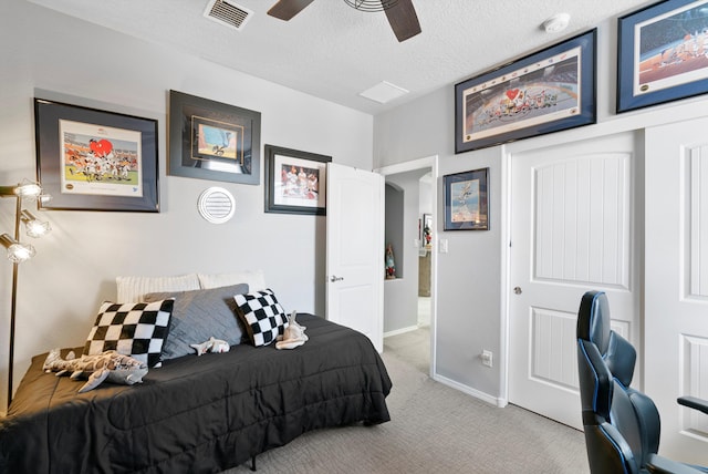 bedroom with a closet, light colored carpet, visible vents, a ceiling fan, and a textured ceiling