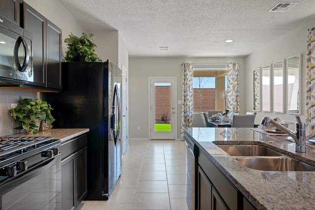 kitchen with visible vents, backsplash, stone countertops, a sink, and black appliances