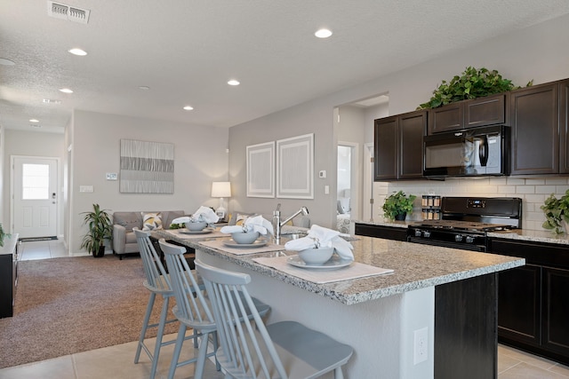 kitchen with a breakfast bar area, light carpet, visible vents, open floor plan, and black appliances