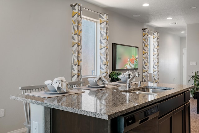 kitchen with black dishwasher, light stone countertops, a textured ceiling, dark brown cabinets, and a sink