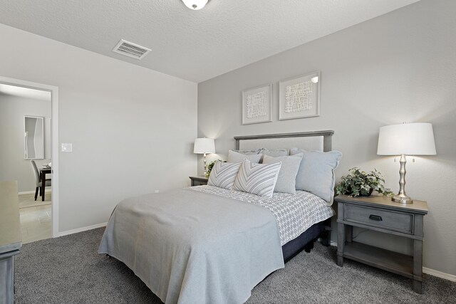 carpeted bedroom with a textured ceiling, visible vents, and baseboards