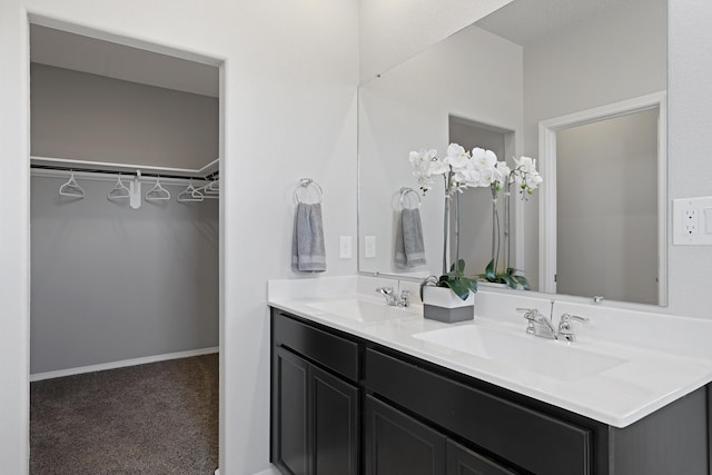 full bath with double vanity, a spacious closet, baseboards, and a sink