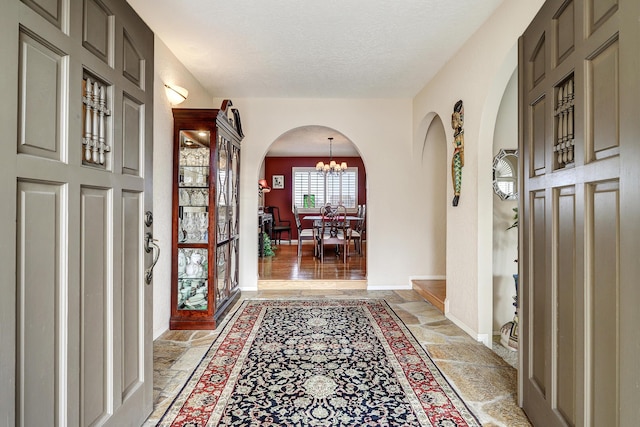 entryway with arched walkways, a notable chandelier, stone tile flooring, a textured ceiling, and baseboards