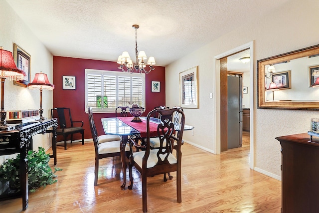 dining area featuring light wood-style floors, baseboards, a chandelier, and a textured ceiling