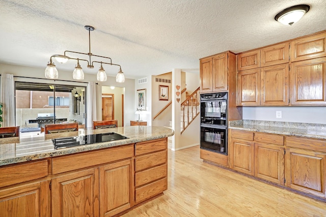 kitchen featuring light wood-style floors, hanging light fixtures, light stone countertops, black appliances, and brown cabinetry