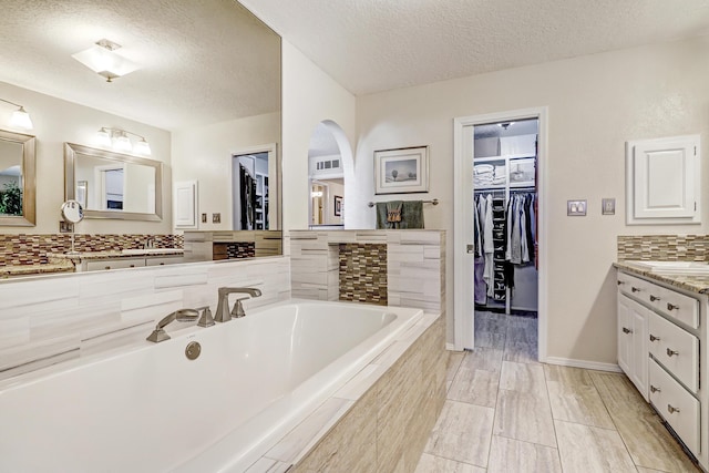 bathroom featuring a textured ceiling, tiled tub, a walk in closet, and vanity