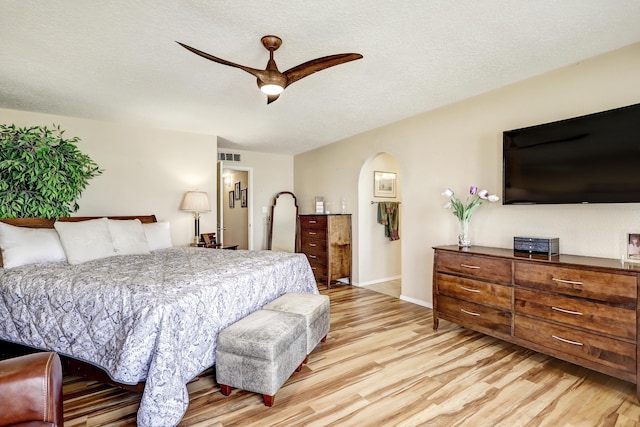 bedroom featuring arched walkways, visible vents, light wood-style flooring, ceiling fan, and a textured ceiling