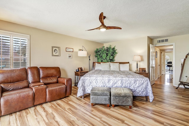 bedroom with light wood finished floors, visible vents, a ceiling fan, a textured ceiling, and baseboards